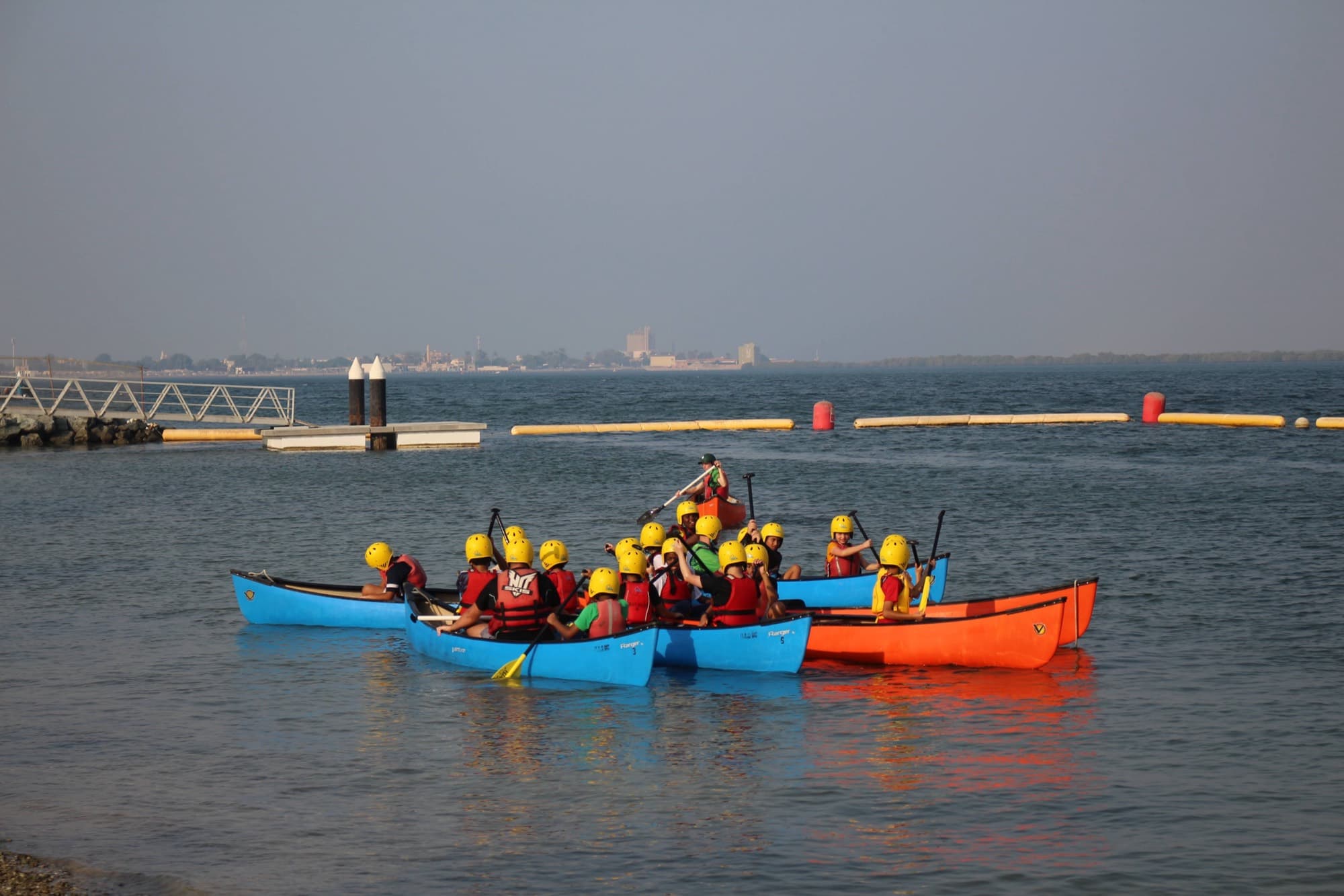 Students paddling canoes together on calm water