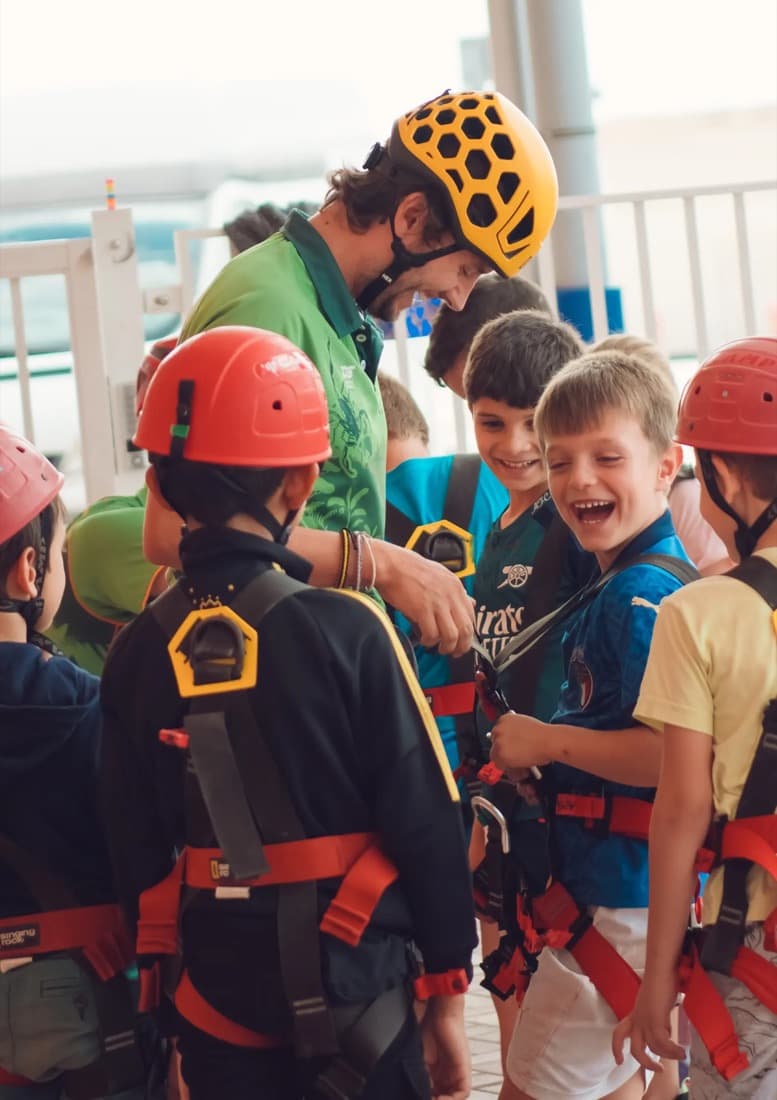 An Ecoventure instructor fitting climbing harnesses on smiling children